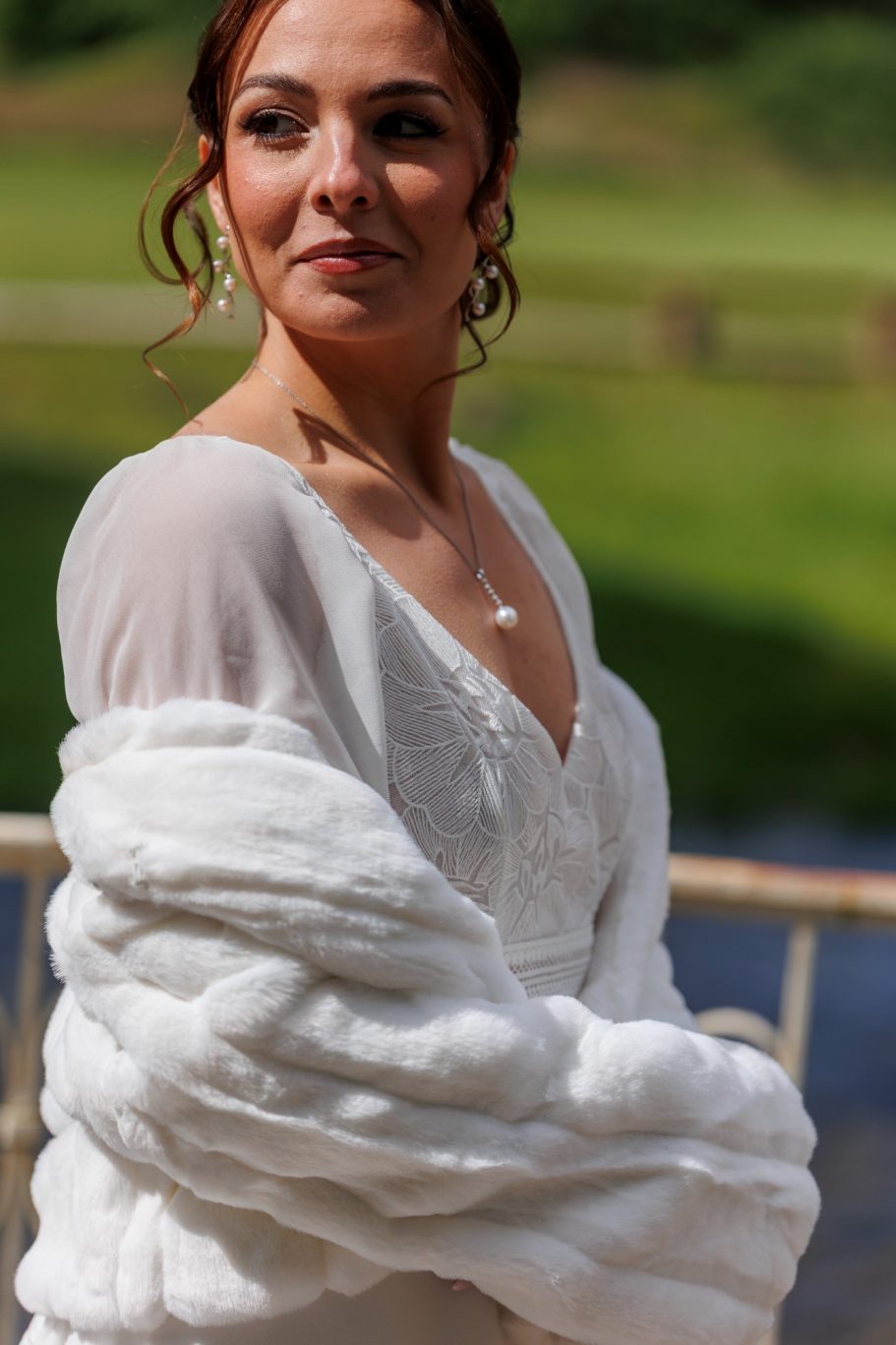 Femme en robe de mariée avec un châle blanc, souriante et regardant au loin.